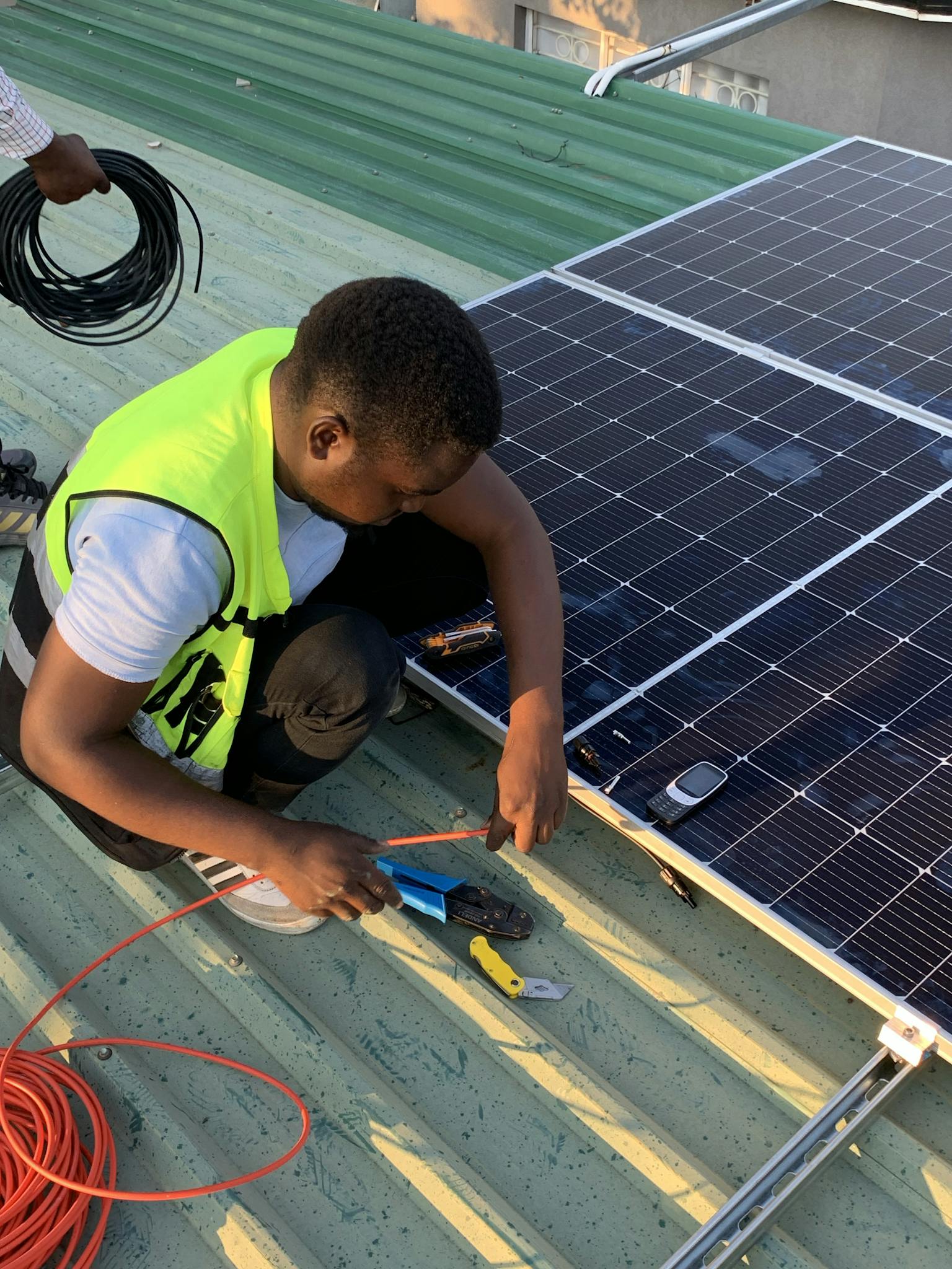 Technician working on solar panel installation with cables and tools on a sunny day.